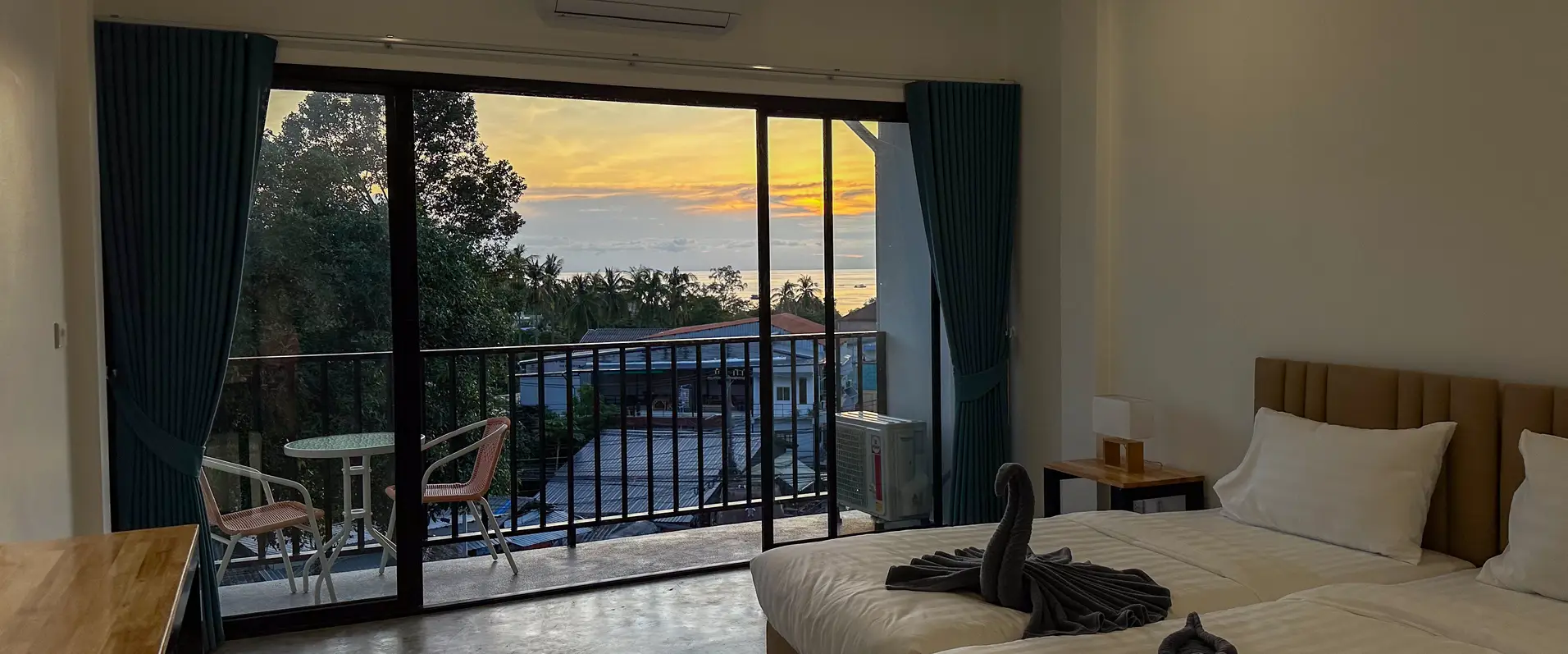 A twin room at dusk, the balcony door open onto the sunset over the sea