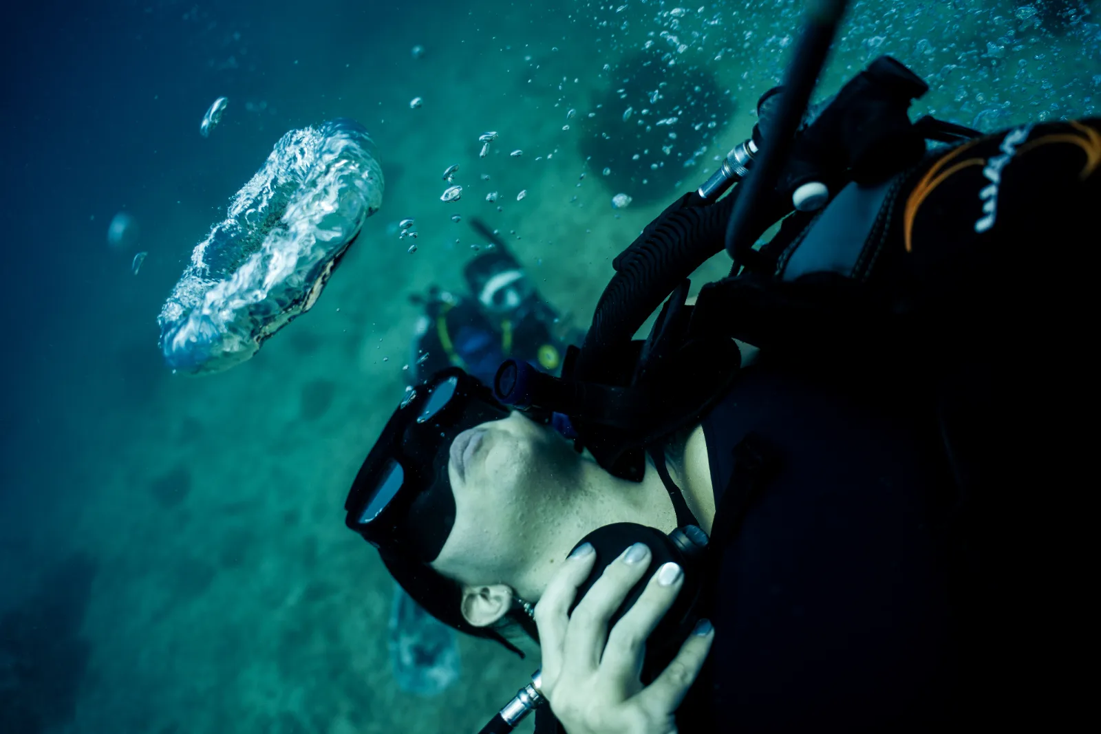 A diver hovering on his back in mid-water, watching a bubble ring rise