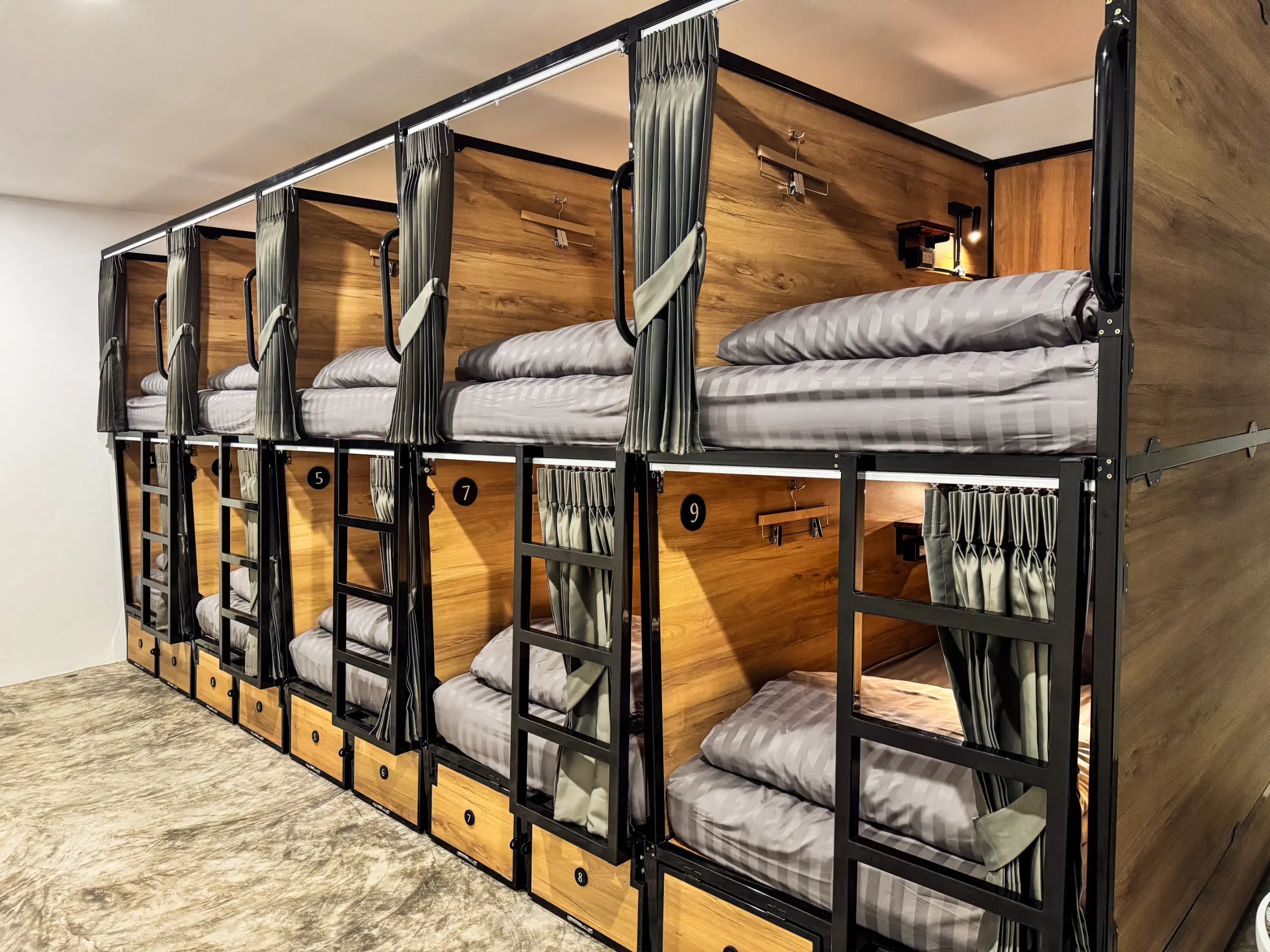 Row of numbered wooden capsule pods with privacy curtains and storage drawers